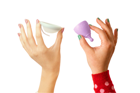 Hand with pink fingernails holding a menstrual disc in the air and a hand with green fingernails holding a lilac menstrual cup in the air on a transparent background