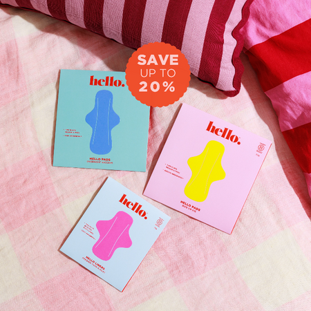 Three colourful boxes of Hello Period panty liners and pads on a pink gingham duvet with and red striped pillows in the background fabric background with a discount graphic icon.