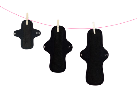 Reusable liner and two reusable pads on a washing line pegged with three wooden pegs