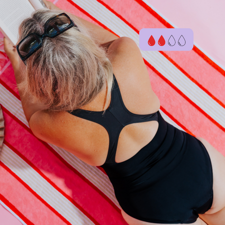 Woman wearing a black cross back period swimsuit lying on a red and white striped towel