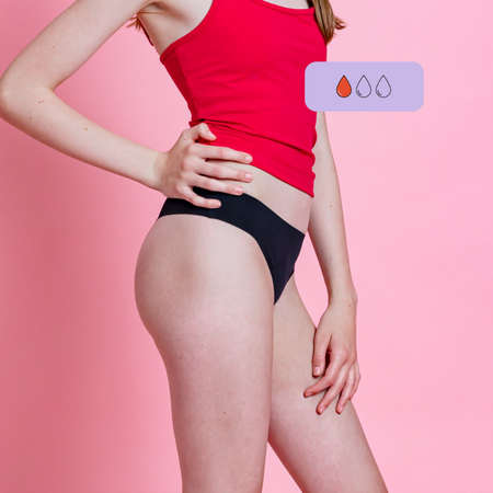 Side profile of woman wearing a red top and black period thong with hand on her hip on a pink background