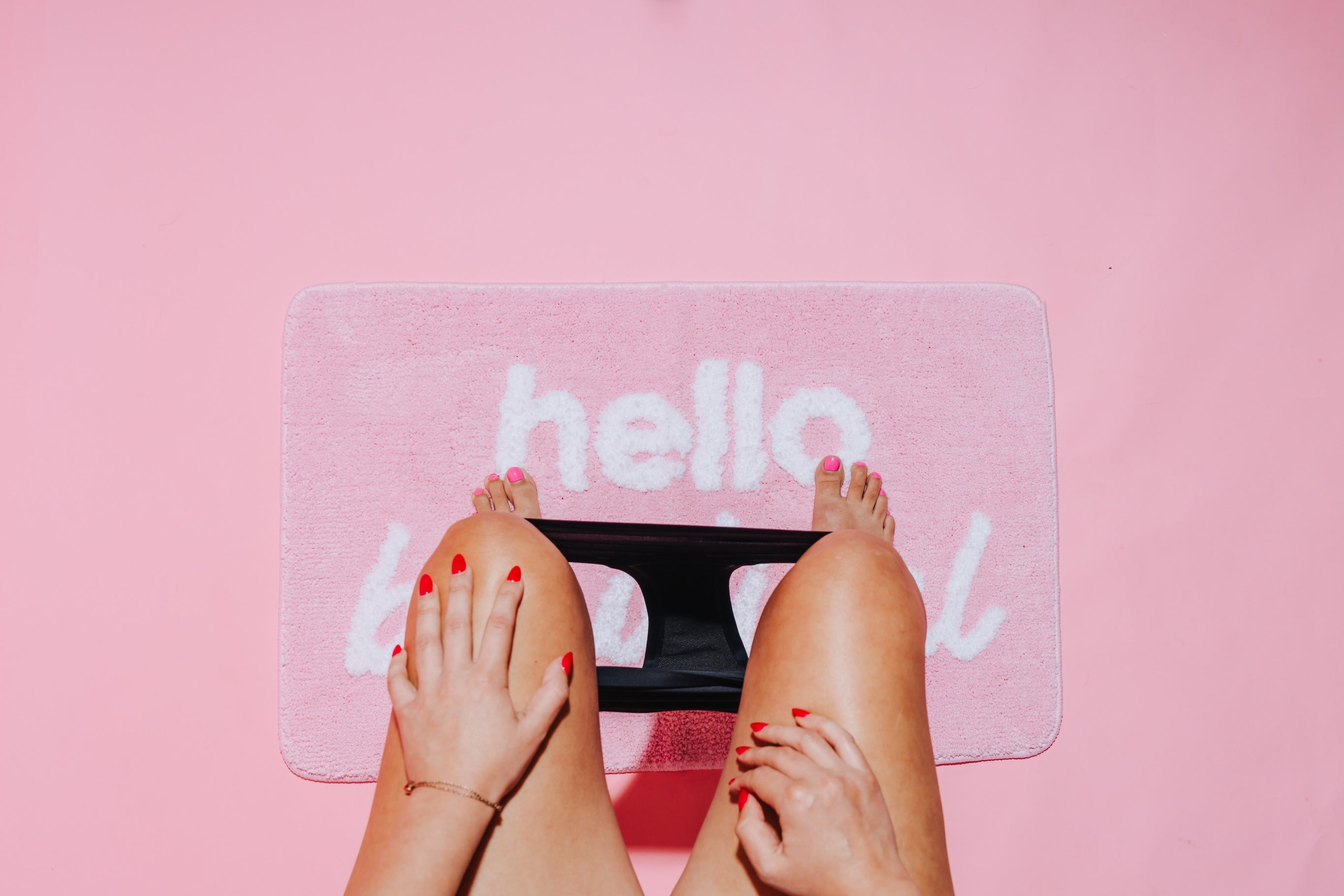 legs with period underwear around ankles and feet on a pink bathmat with a pink background