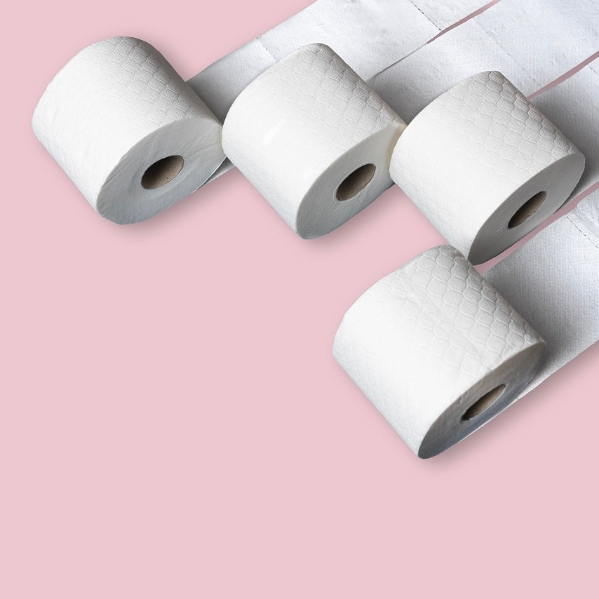 four rolls of white toilet paper on a soft pink background