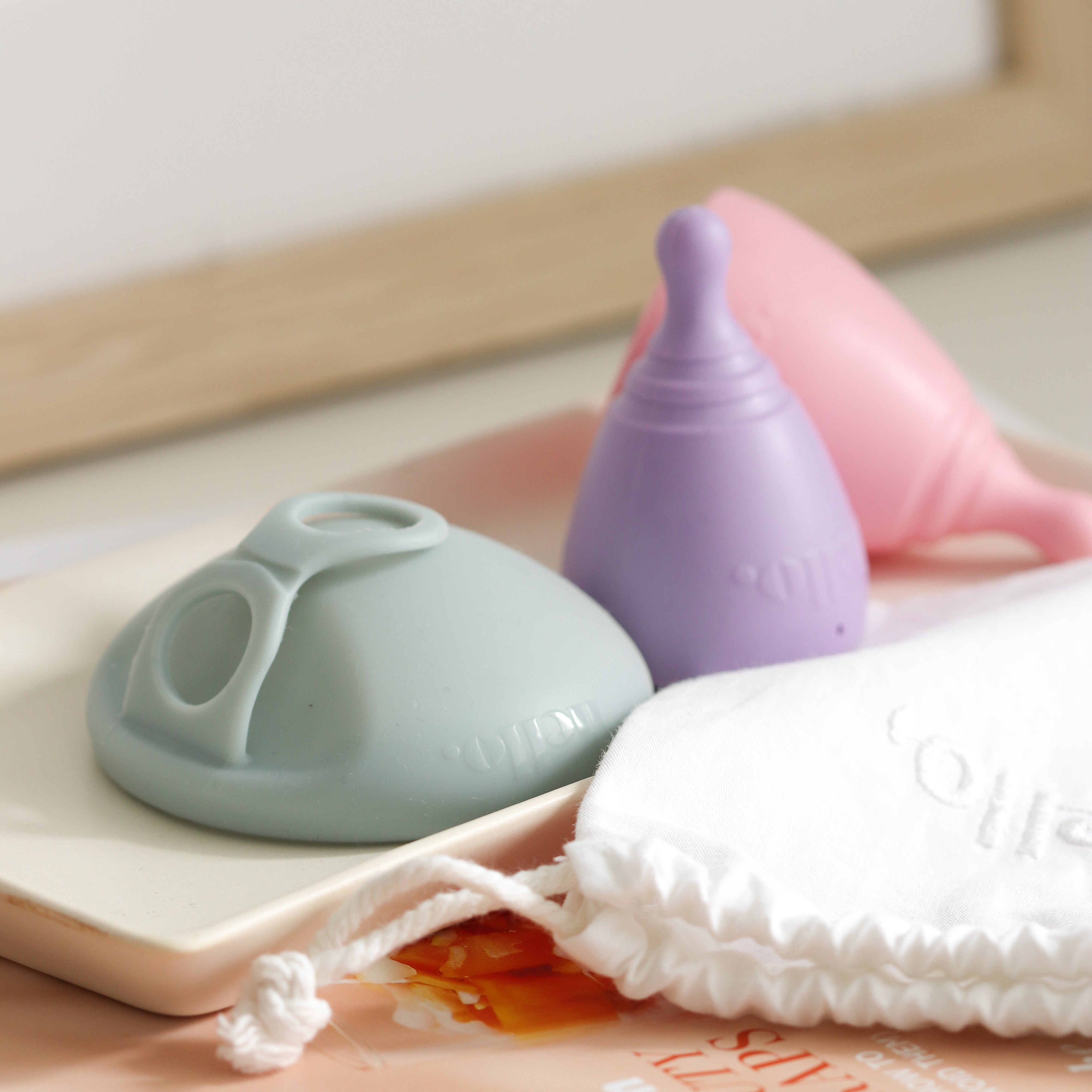 Menstrual disc by Hello Period and two menstrual cups in various colours