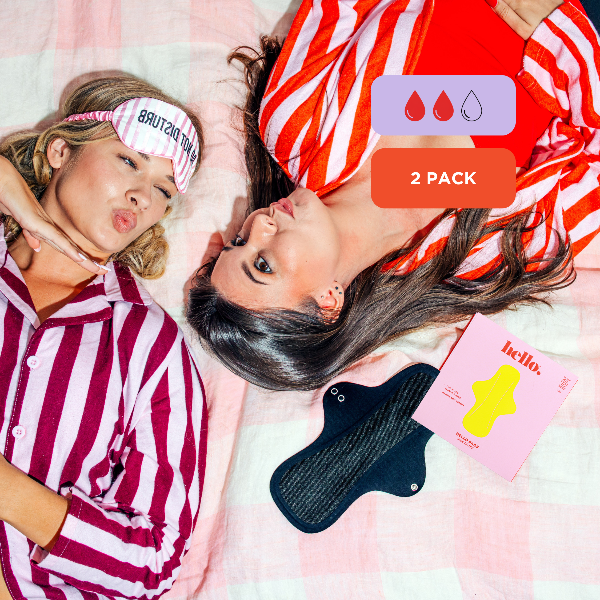 Two women in matching striped pyjamas with a black sanitary pad and pink packaging on a bed.