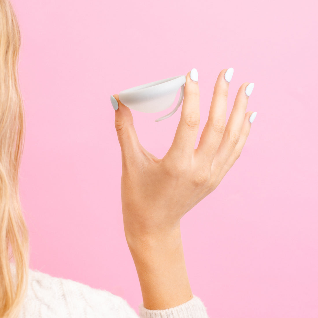 Hand holding a sea fog menstrual disc by Hello Period against a pink background