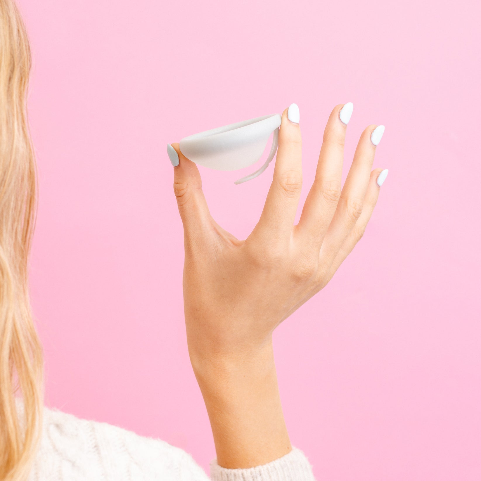 Hand holding a sea fog menstrual disc by Hello Period against a pink background