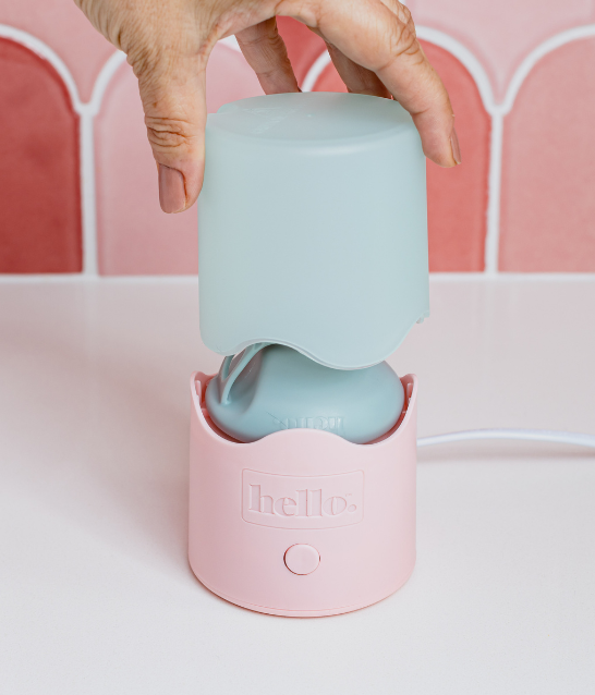 Hand lifting the lid of Hello Steamy steam steriliser with pink tiled wall in background