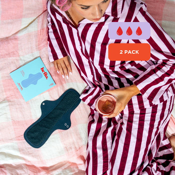 Person in a striped pyjama lying on a bad with a gingham duvet cover and a black Overnight Success pad by Hello Period on the bed next to her alongside a blue packet with featuring a blue pad illustration. There are 2-pack and absorbency graphic icons. 