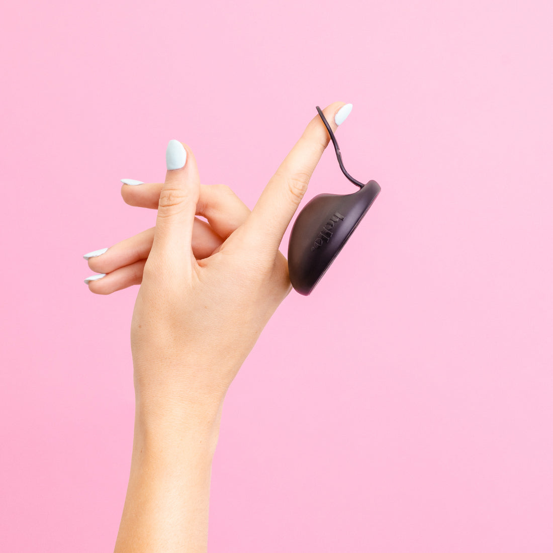 Hand holding a black menstrual disc  against a pink background