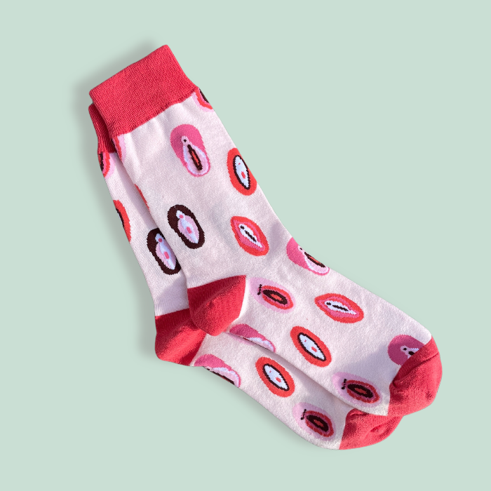 A pair of socks with vulva illustrations on them in a flat lay on a green background 