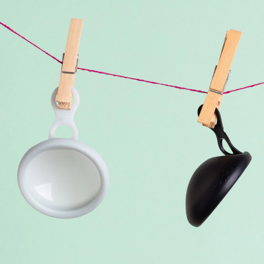 blue menstrual disc and black menstrual disc on a clothesline attached by wooden pegs with a soft green background